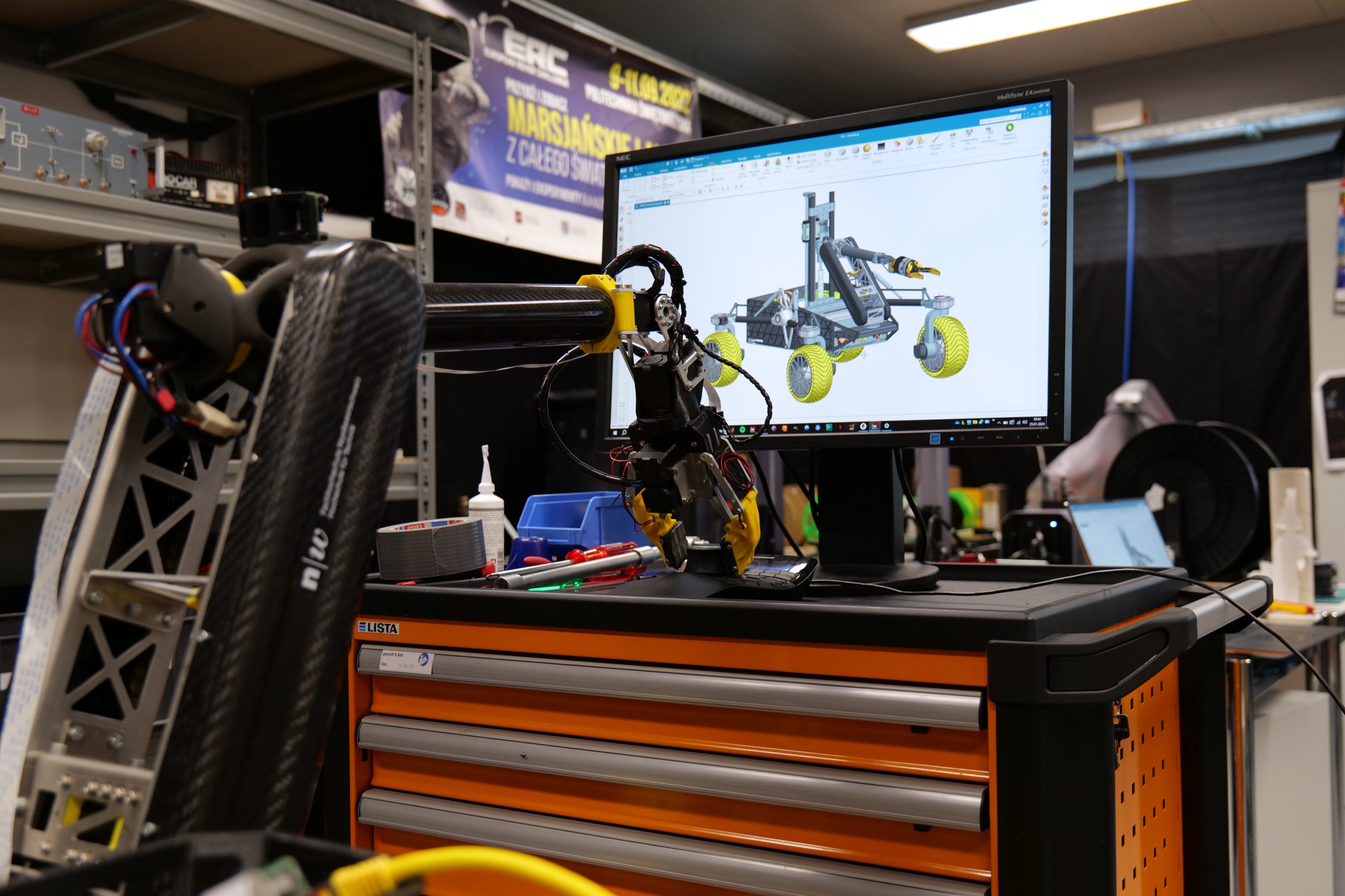 The FHNW Rover's carbon-fibre manipulator arm in the workshop, its CAD model glowing on the monitor behind